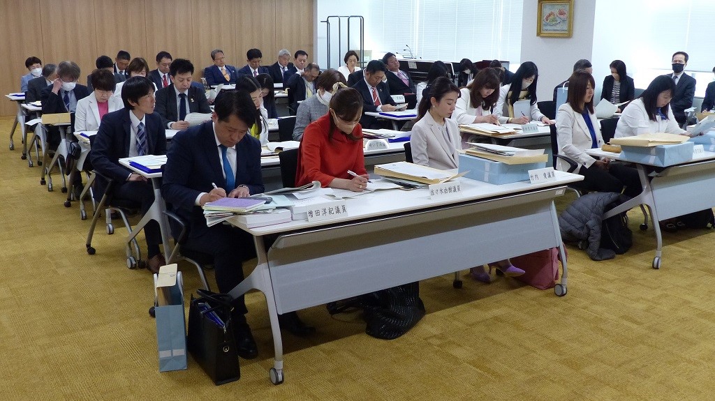 写真：会議室にて区議会説明会を受ける議員の様子を前から撮影