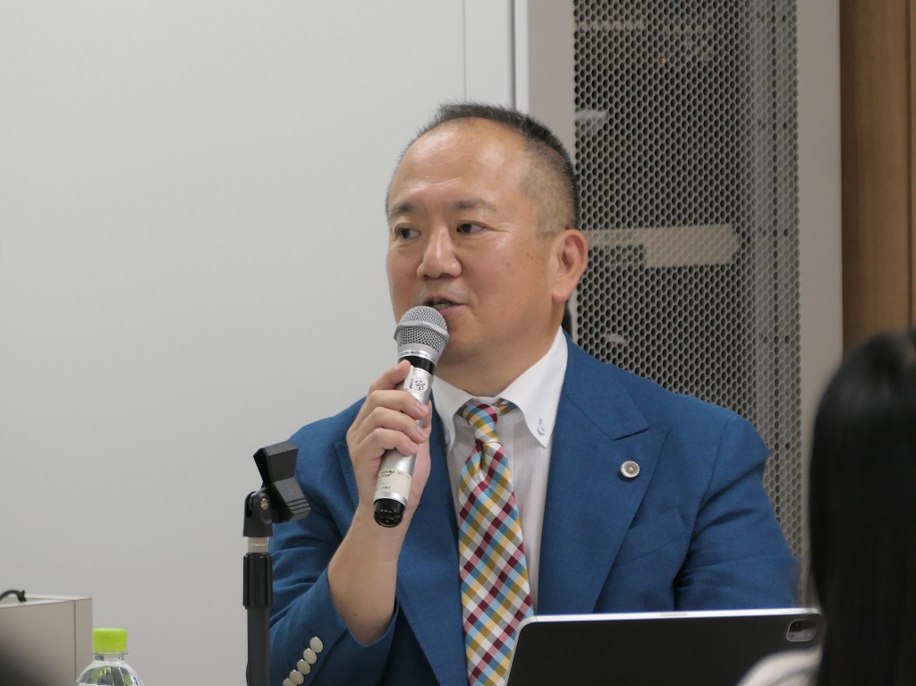 写真：マイクを持って講義をする　いりさわ たけひさ氏の様子